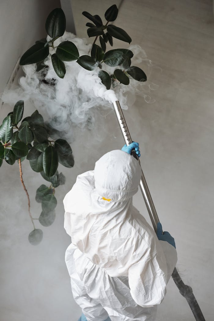 About A person in protective gear uses a sprayer for indoor disinfection.